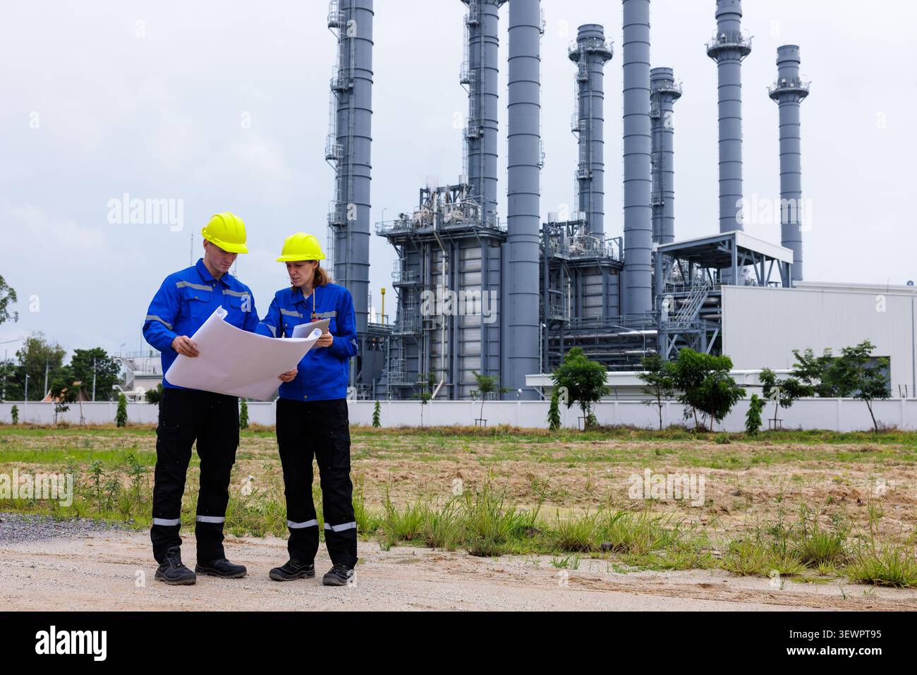 Two engineers in safety helmets and uniforms discuss project plans at a power generating facility. Stock Photo