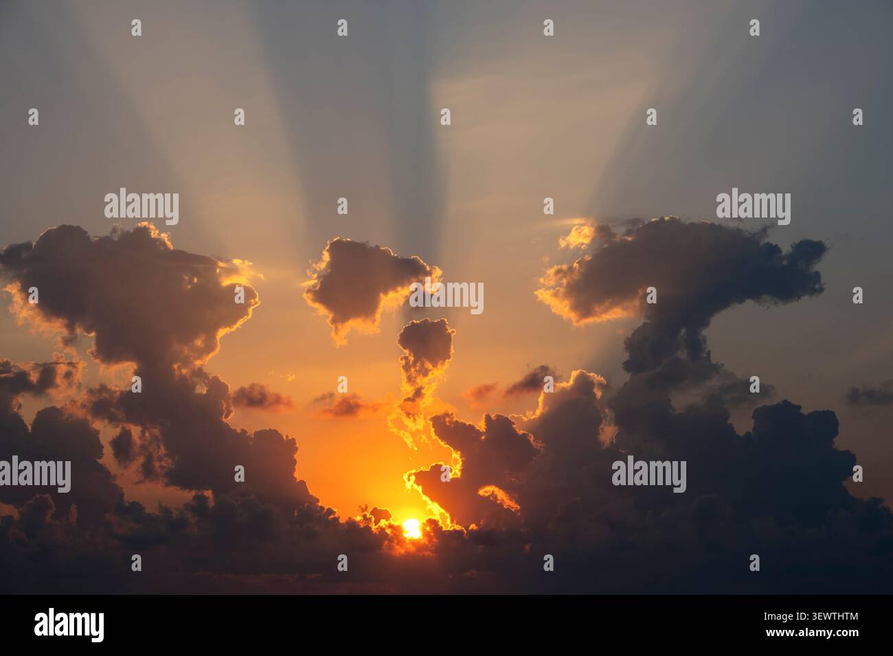 Sun setting behind dark clouds with dramatic golden crepuscular light rays Stock Photo