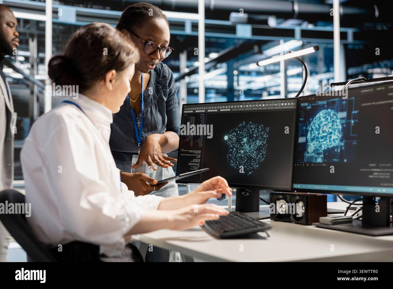 System administrators use a computer in a server hub to visualize AI neural networks and brainstorm system oversight. Stock Photo