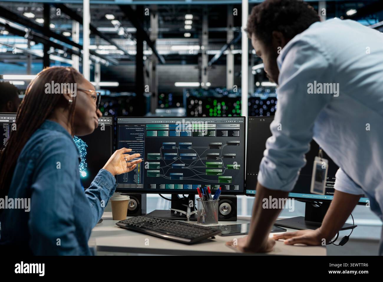Manager supervises a technician coding in a server farm, overseeing repairs on data center racks used for computational operations. Stock Photo