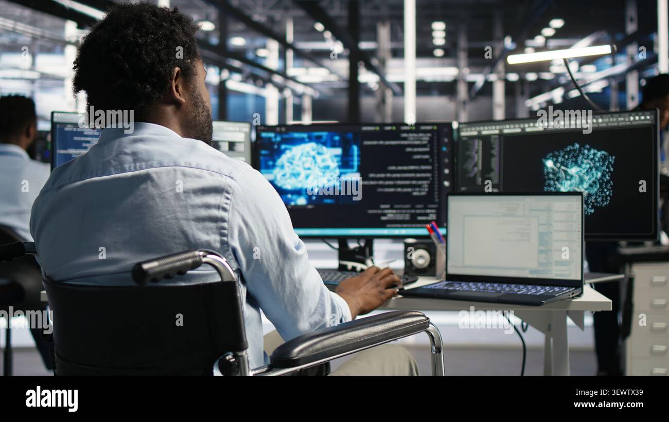 Computing hub software programmer with paraplegia in wheelchair operates AI machine learning visual programming system with man with disability in inclusive server facility assesses equipment issues. Stock Photo