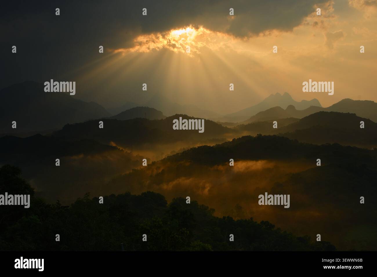 Dramatic Sunbeams Breaking Through Dark Clouds Over Misty Mountain Landscape Stock Photo