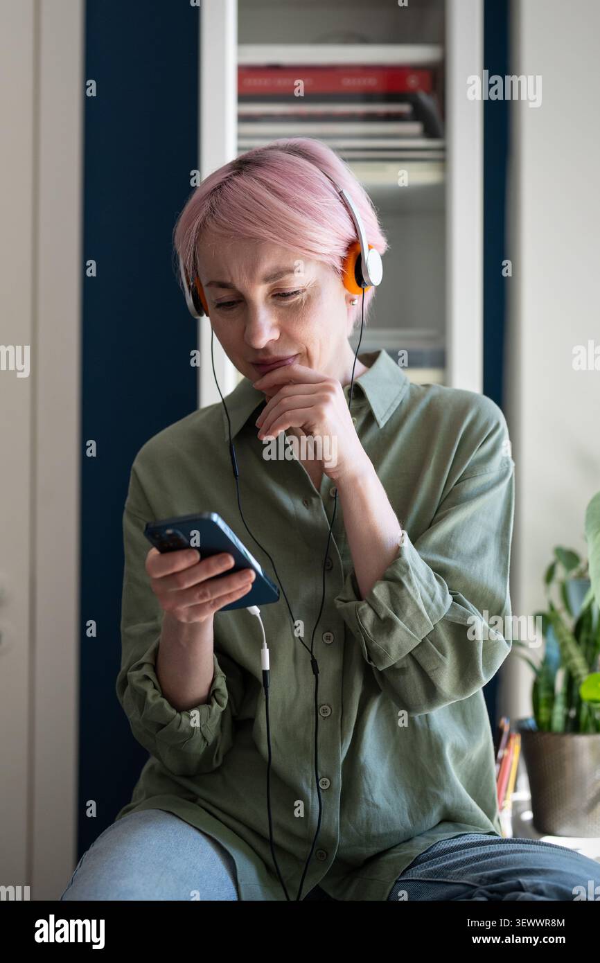 Interested thoughtful mature woman enjoying listening to music and podcasts online using mobile app. Stock Photo