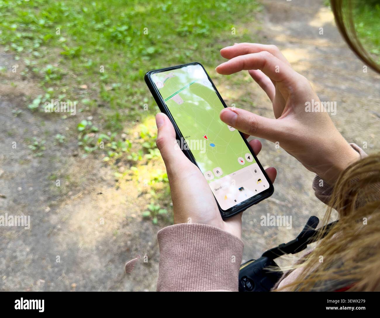 Hands use smartphone map application in outdoor setting. Person navigates forest using digital interface on screen. Technology concept reflects naviga Stock Photo