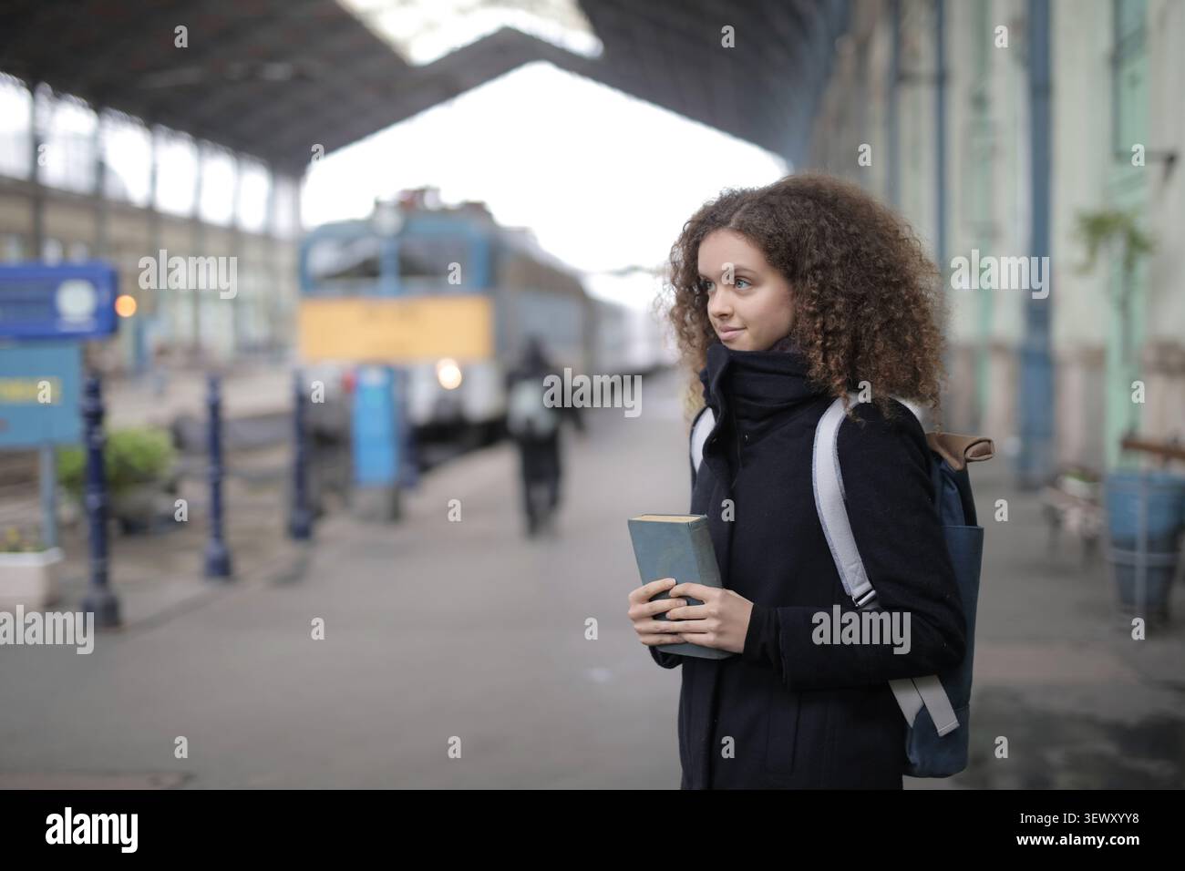 Thoughtful woman holding a book on a train platform Stock Photo