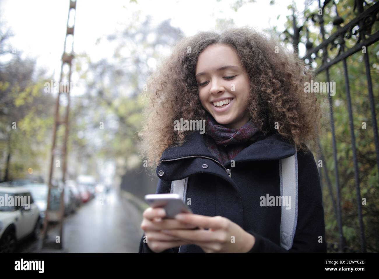 Happy curly haired woman using her smartphone outside Stock Photo