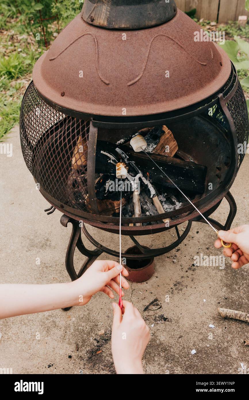 Hands roasting marshmallows over an outdoor fire pit Stock Photo