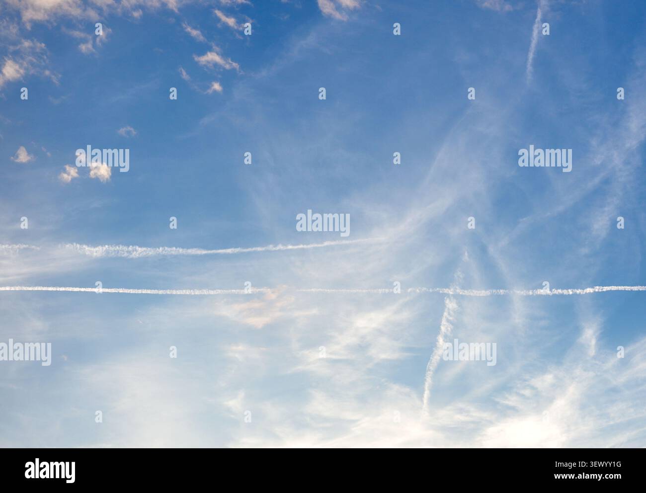 Bright blue sky covered with wispy cirrus clouds and long white airplane contrails stretching horizontally on a pleasant day in Croatia. Stock Photo