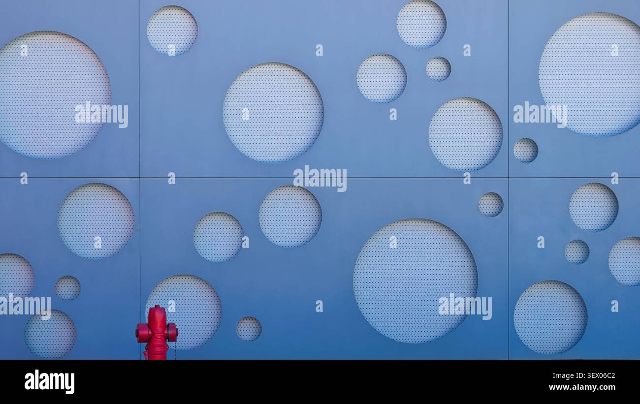 Blue modern facade with circular perforated patterns and a red fire hydrant. Stock Photo