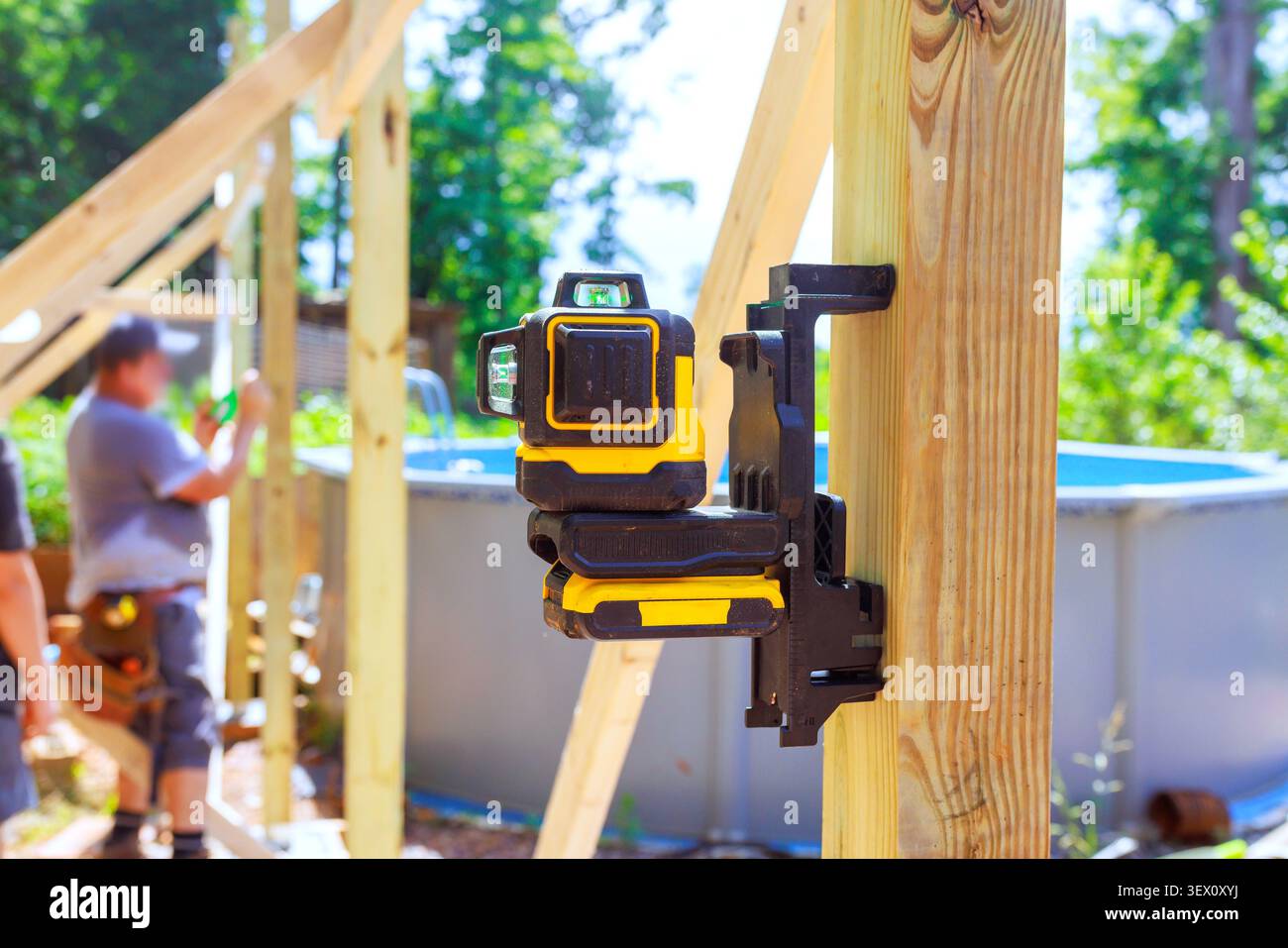 Frame workers are building structure near pool using laser level for accuracy in backyard. Stock Photo
