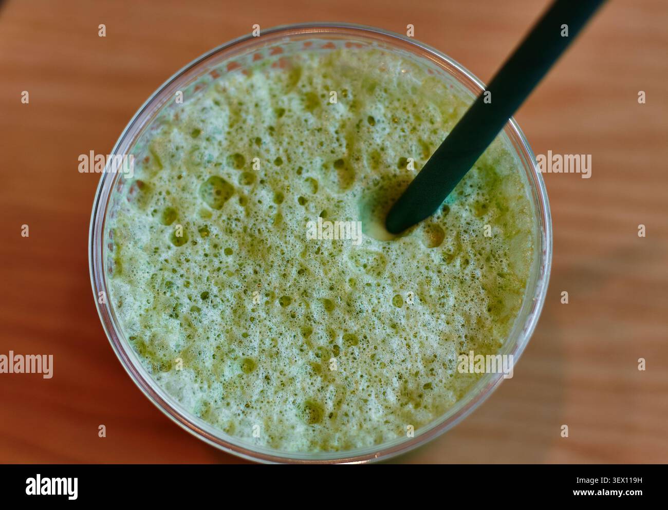 Green iced matcha smoothie served in a clear cup with a green straw, showing bubbles on the surface, resting on a wooden table Stock Photo