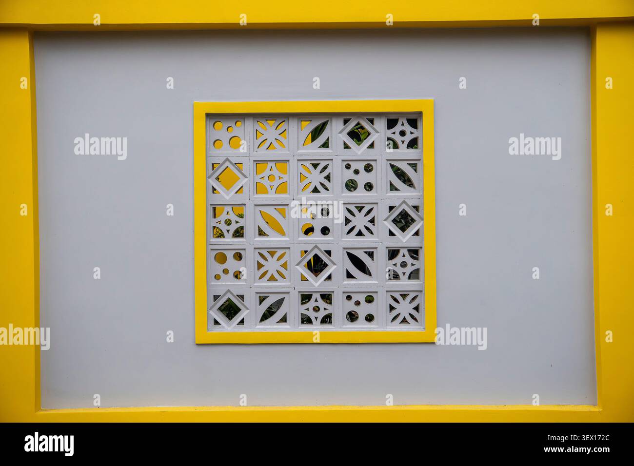 Decorative white concrete breeze block panel with geometric patterns in a yellow frame on grey wall Stock Photo