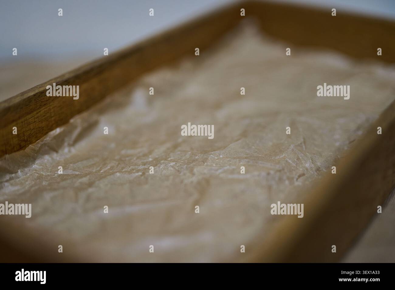 Wooden Tray Lined With Crumpled Parchment Paper Placed On Table Closeup Showing Paper Texture And Wood Grain With Shallow Depth Of Field For Serving Or Packaging Display. Stock Photo