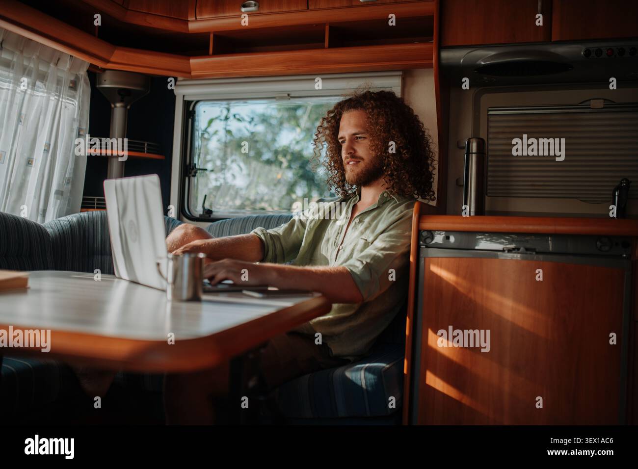 Young man working remotely from caravan. Man using camper as homeoffice, working on notebook. Stock Photo
