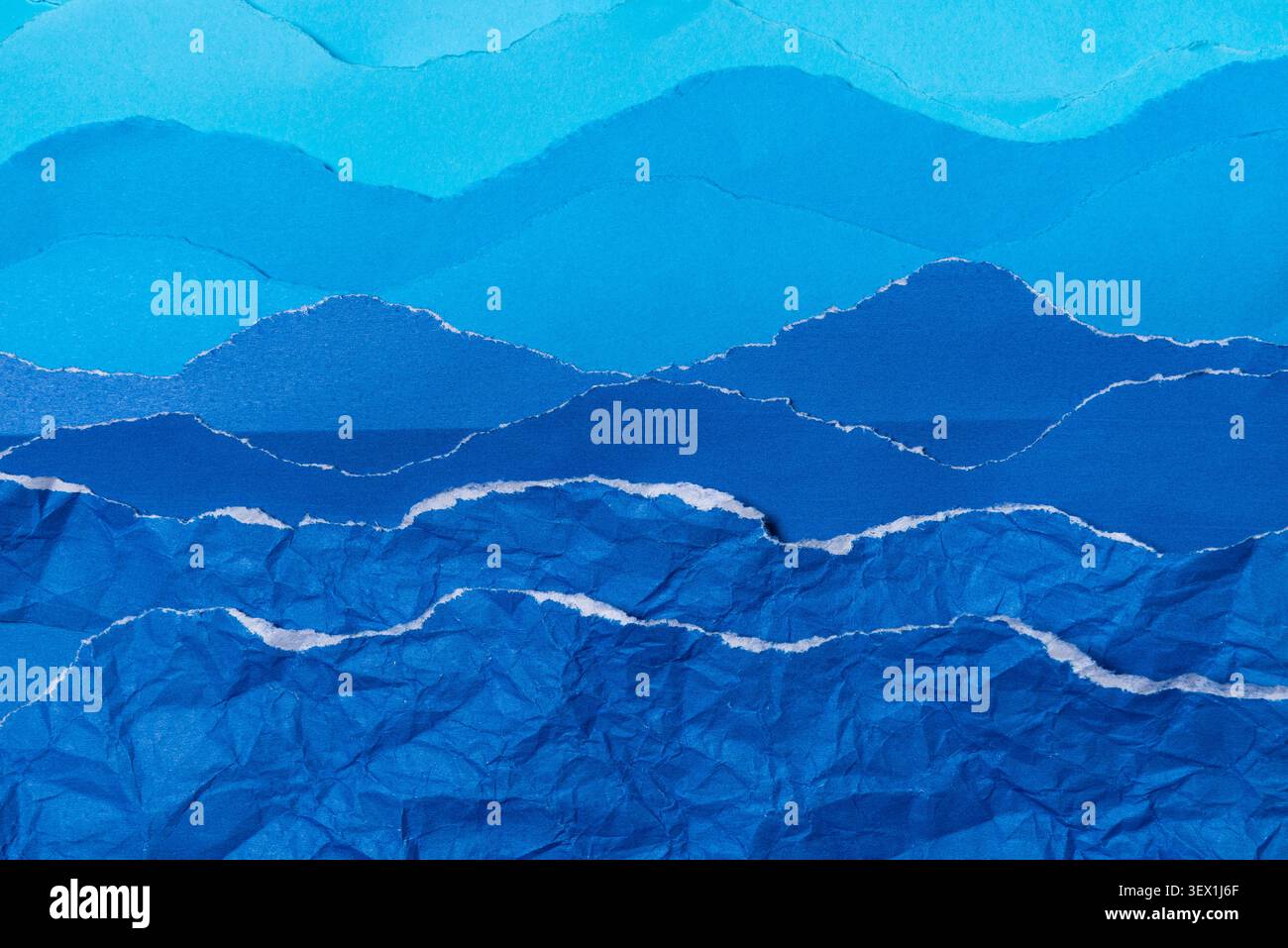 A textured background created from torn layers of blue paper, mimicking the appearance of undulating ocean waves against a serene sky horizon. Stock Photo