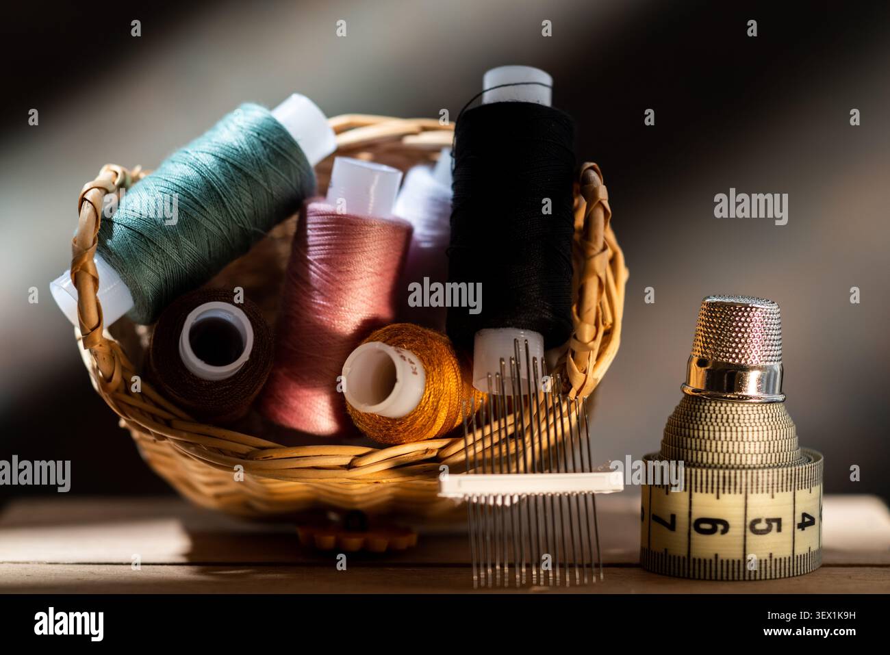 Wicker basket with colorful sewing threads, needles, measuring tape and thimble on a wooden table. Stock Photo