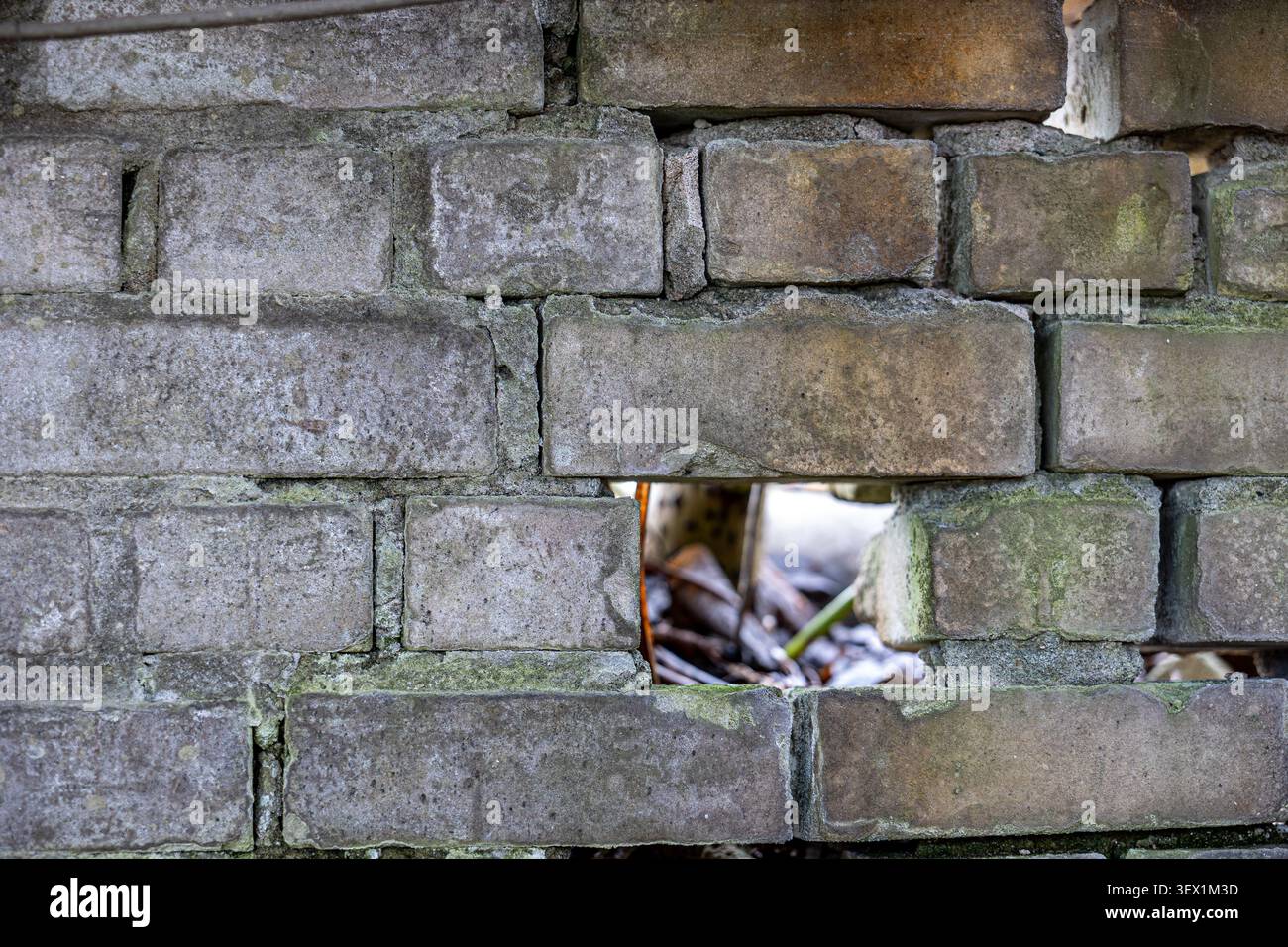 Old, rough brick wall with a distinct rectangular gap where a brick is missing, revealing a blurry background, symbolizing neglected structures, wear, Stock Photo
