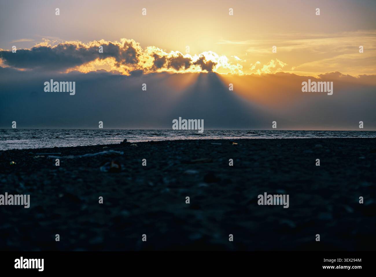 Dramatic sunset over the sea with sun rays breaking through clouds on a dark beach Stock Photo