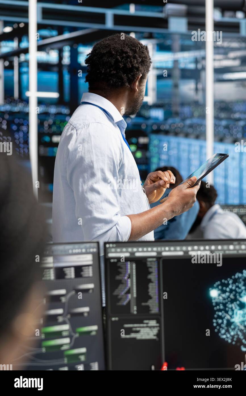 System administrator reviews AI systems and neural network parameters on a tablet inside a data center. Stock Photo