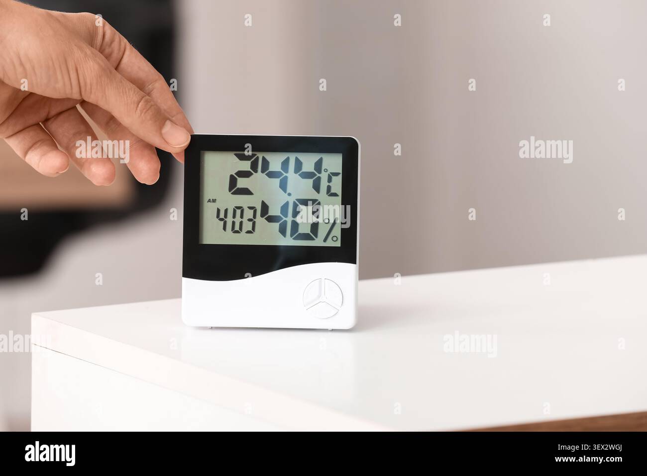 Hand adjusting digital thermometer and hygrometer on table Stock Photo
