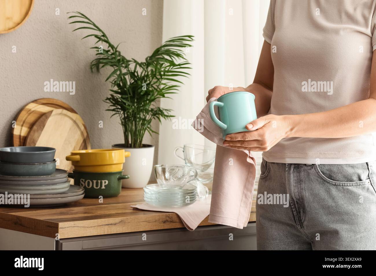 Person drying a turquoise mug in a kitchen Stock Photo