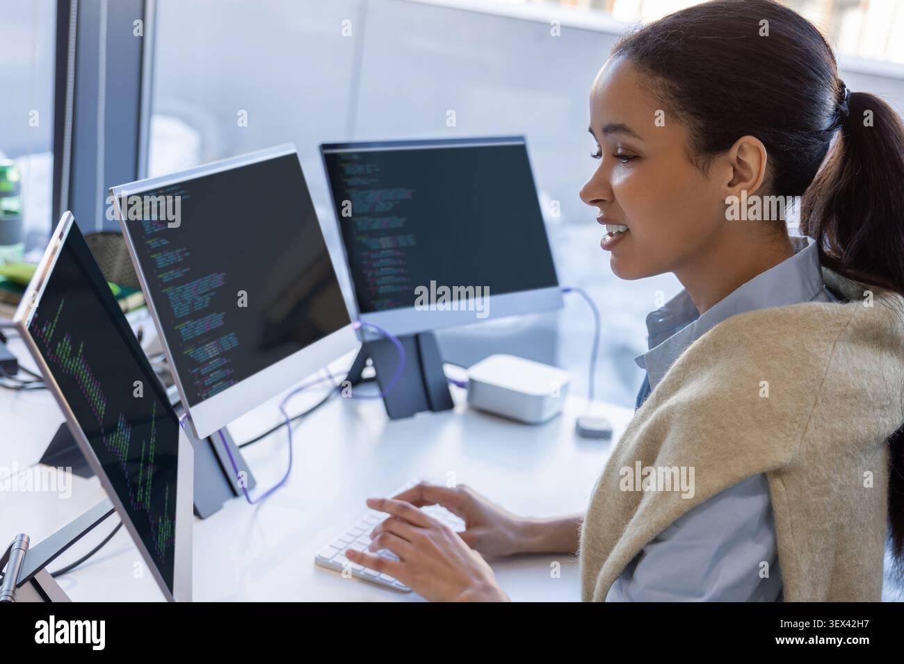 Female developer coding on multiple monitors in office Stock Photo