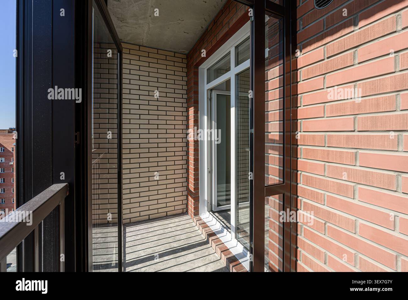 balcony with brick walls, an open white-framed window, and black metal frames. Sunlight casts shadows on the floor Stock Photo