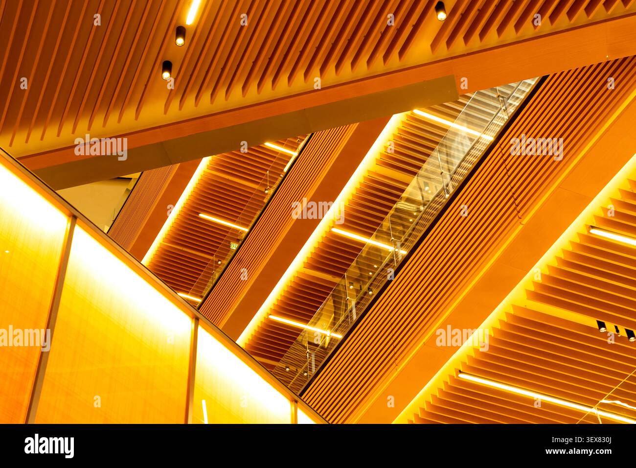 Modern architectural interior featuring abstract wooden geometric ceilings and warm linear lighting. Stock Photo