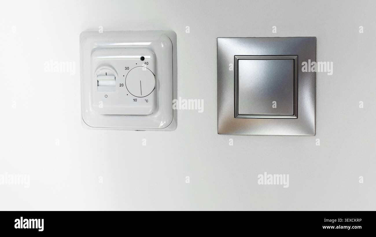 Mechanical room thermostat and modern light switch on wall Stock Photo