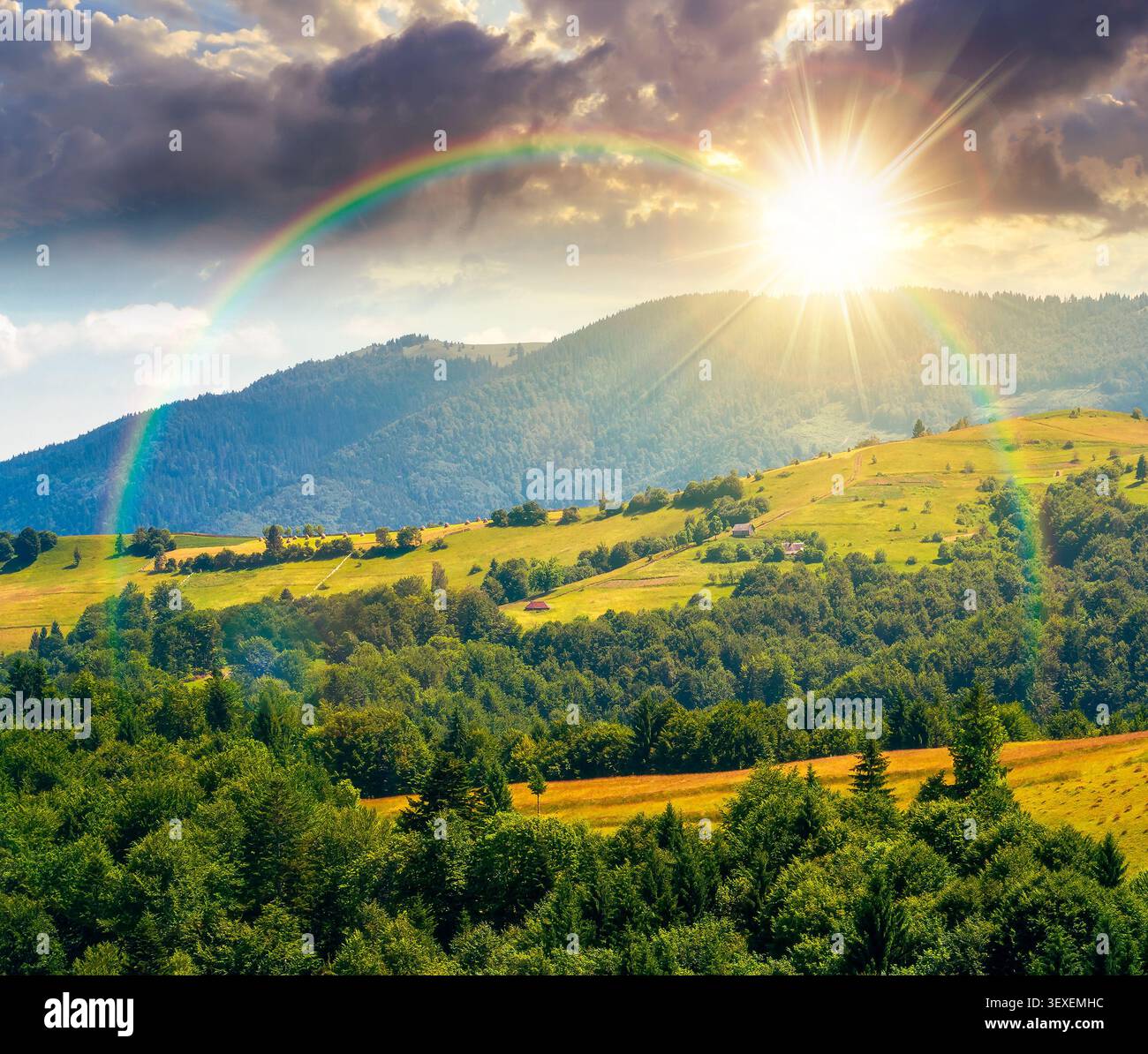 sunset over agricultural field on hillside in mountains near village. summer evening. green carpathian mountain landscape. narrow view. remote alpine Stock Photo