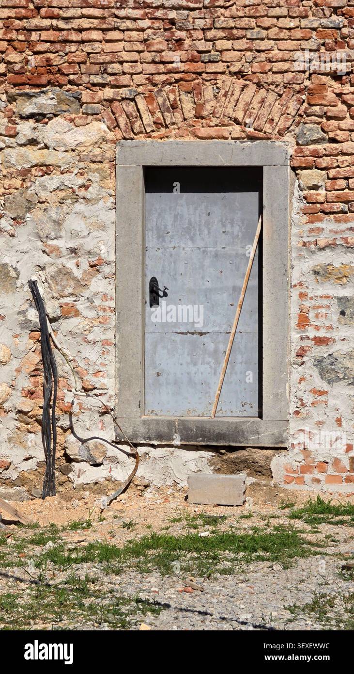 A vertical close-up shot displays a closed grey iron door framed by massive cut stones under a historic arched brick header Stock Photo