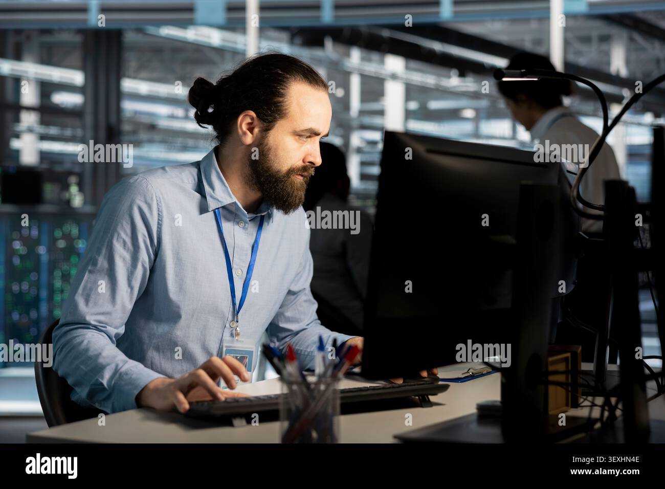 System administrator uses a desktop computer in a data center to manage AI systems and optimize server infrastructure. Stock Photo