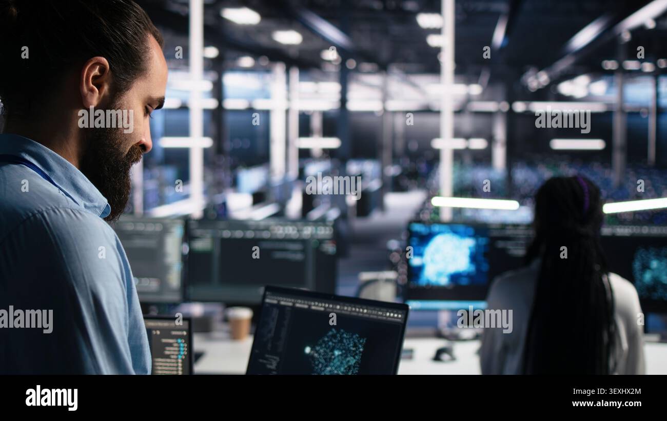 Computing facility software programmer working with notebook to track neural network working with AI large language model chatbot with working with AI on notebook to oversee servers powering machine. Stock Photo