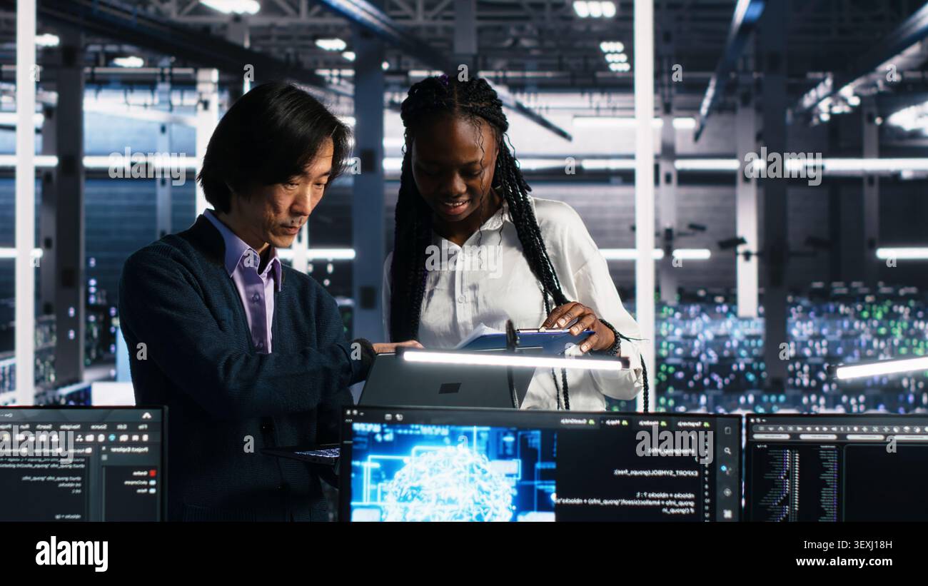 Data center engineers review paperwork while using deep learning algorithms to analyze datasets and recognize patterns in a server farm. Stock Photo