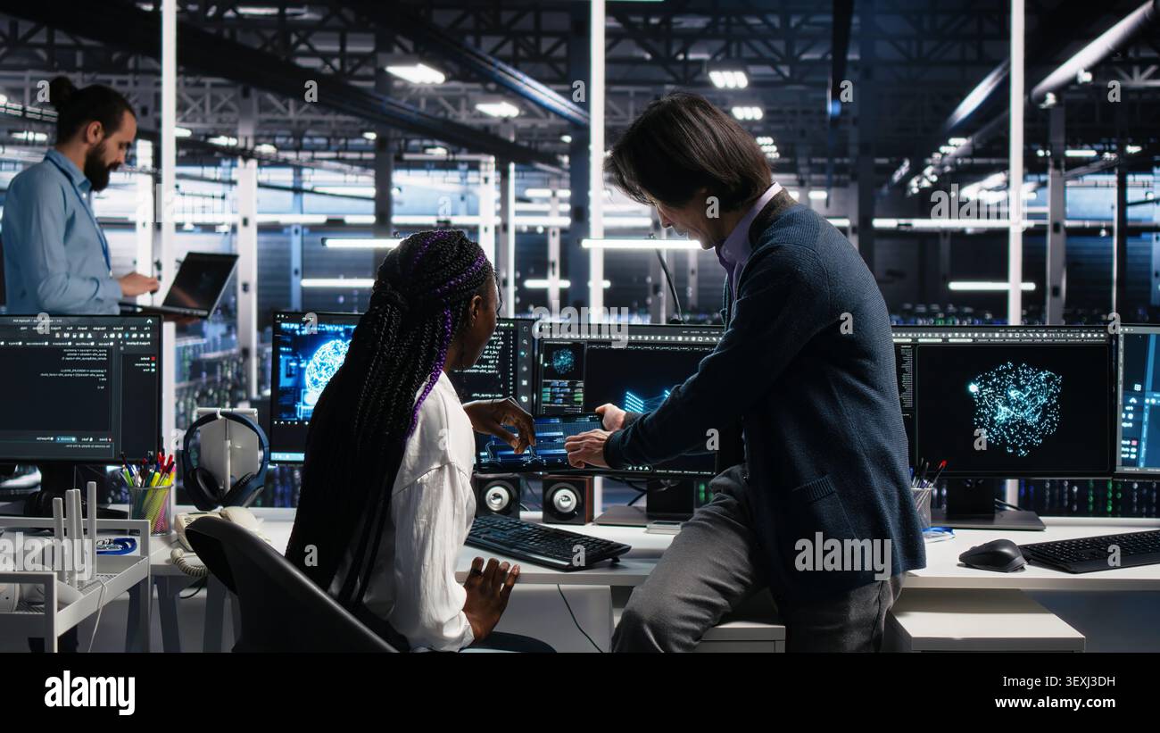 Senior engineer and trainee develop neural network software in a data center, using a PC to implement machine learning technology. Stock Photo