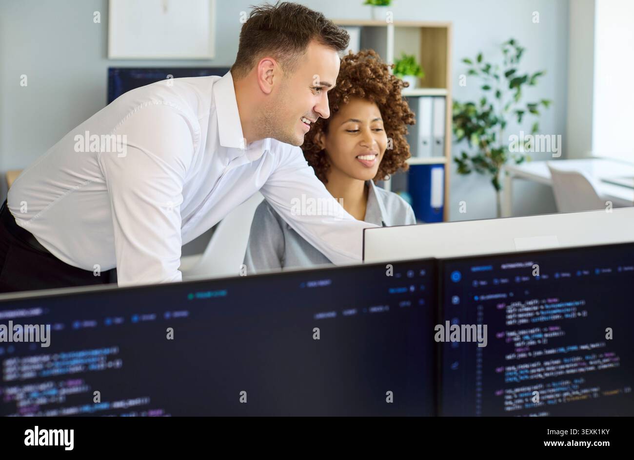 Developers collaborating at computer screens in modern office, coding and mentoring Stock Photo