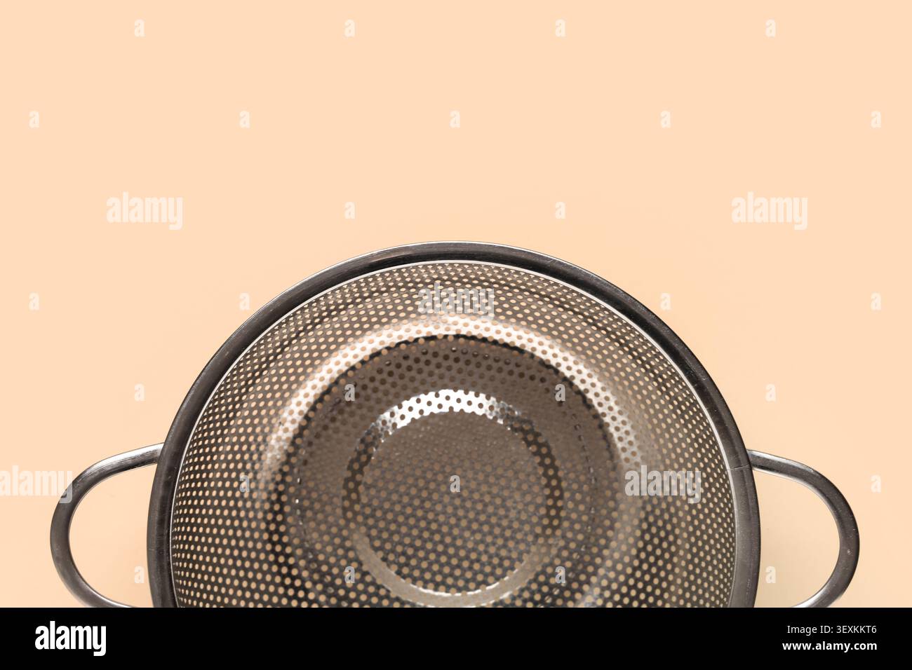 Empty metal kitchen colander on peach background Stock Photo