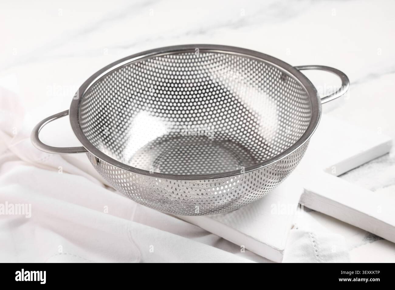 Empty stainless steel kitchen colander on white cloth Stock Photo