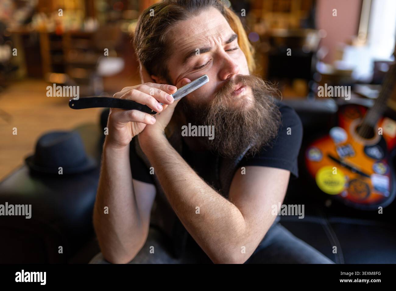Bearded master leaning back on a leather sofa with a straight razor Stock Photo