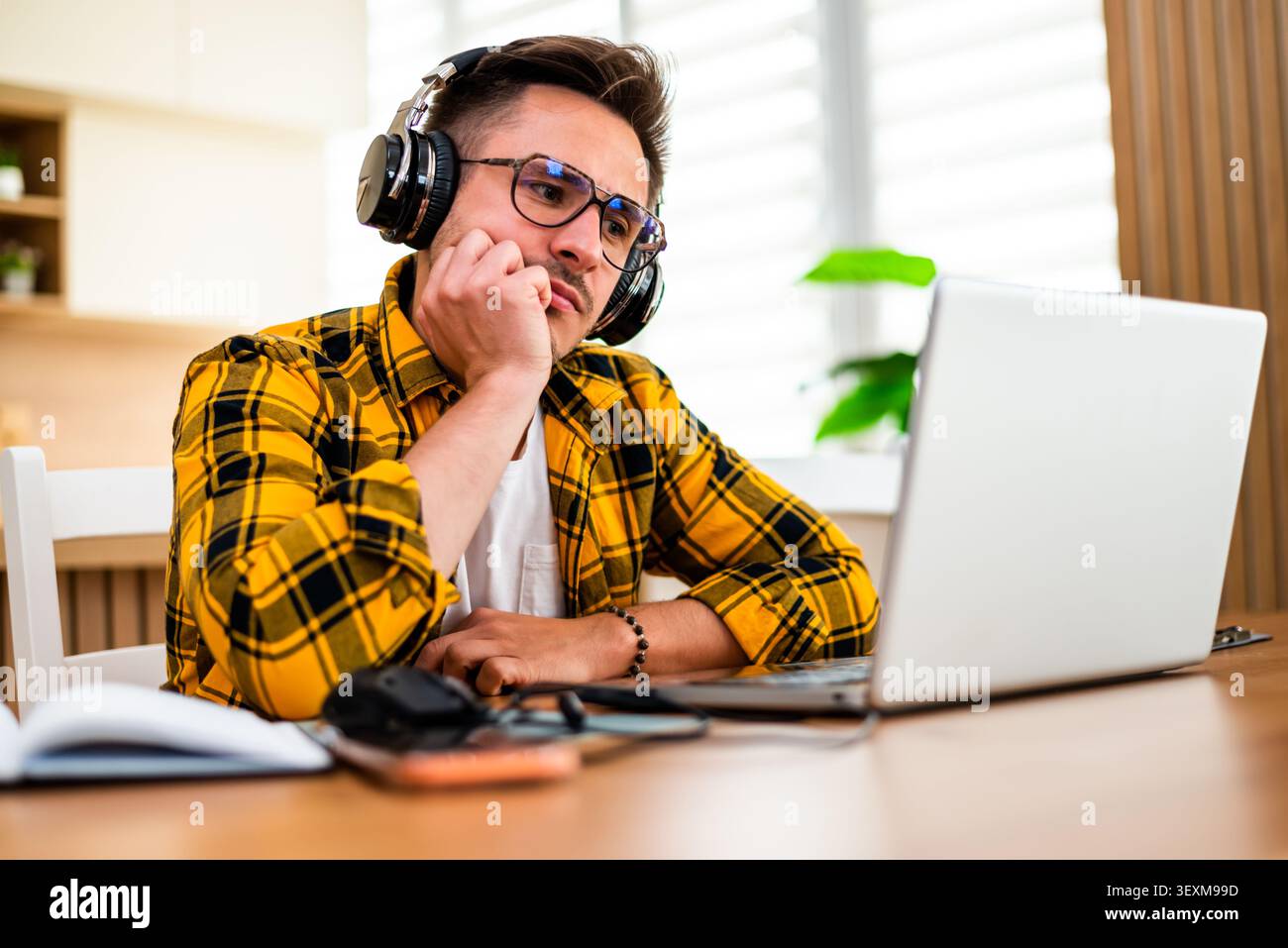 With a pensive and worried expression, a man works on his laptop, appearing to analyze information or solve a problem online. Stock Photo