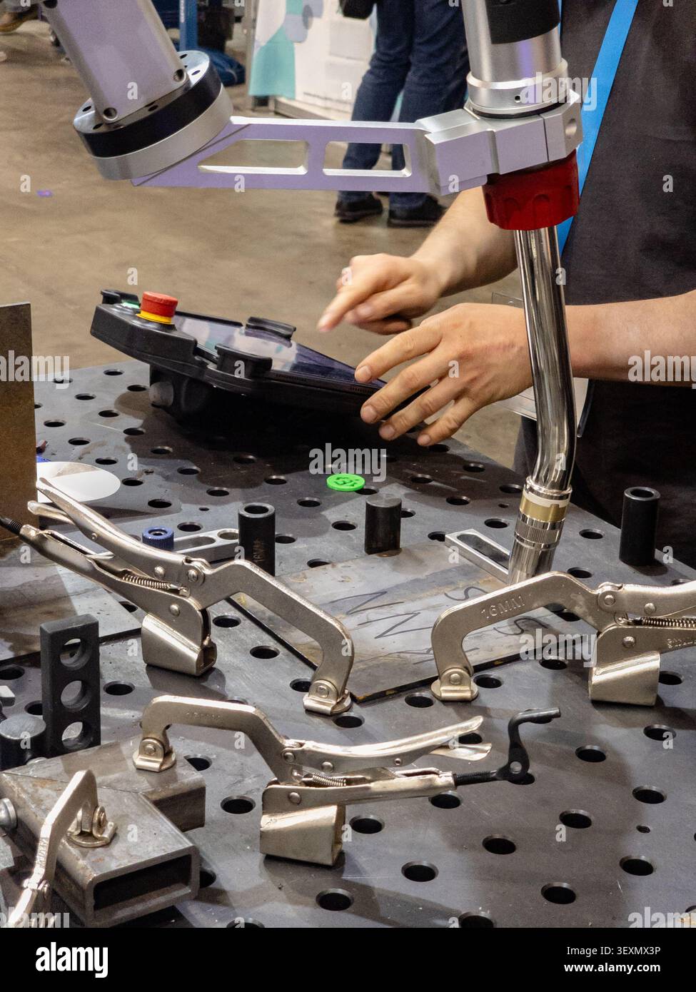An industrial technician programs a collaborative robotic welder using a touch screen control panel, with metal locking clamps securing the workpiece Stock Photo
