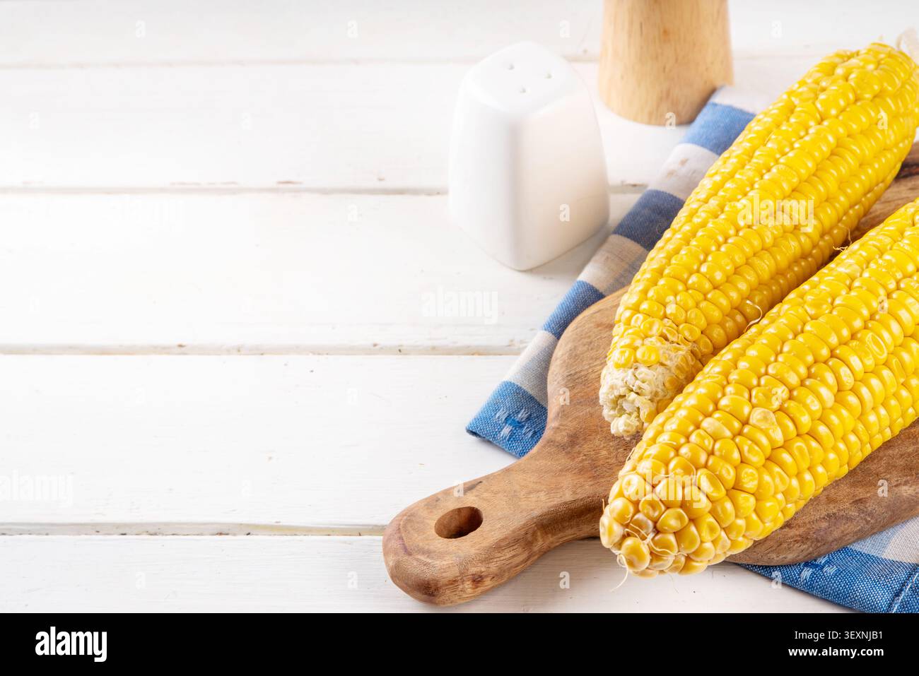 Sweet boiled corn cobs portions on plate, with salt and spices, on white wooden table copy space Stock Photo