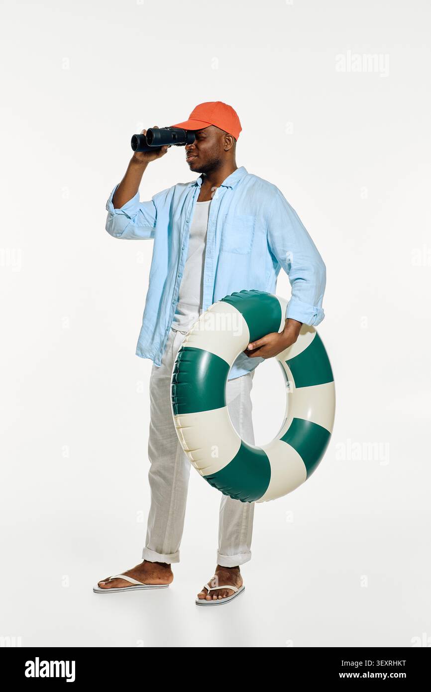 Stylish man stands near the beach holding a lifebuoy, ready for summer adventures and fun. Stock Photo