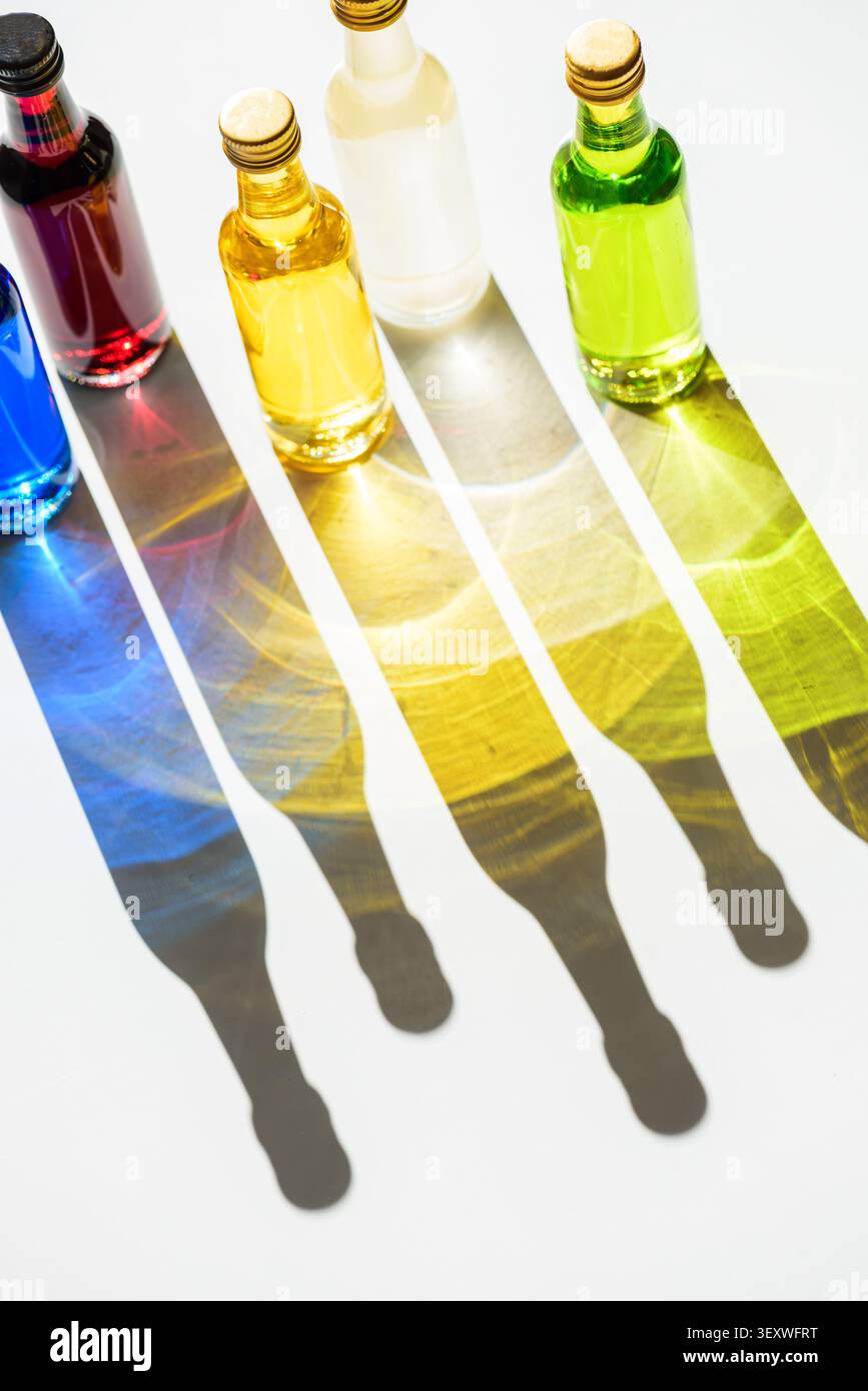 Row of small glass bottles filled with blue, red, yellow, off-white, and green liquids, creating long, vivid color and light refractions on a white su Stock Photo