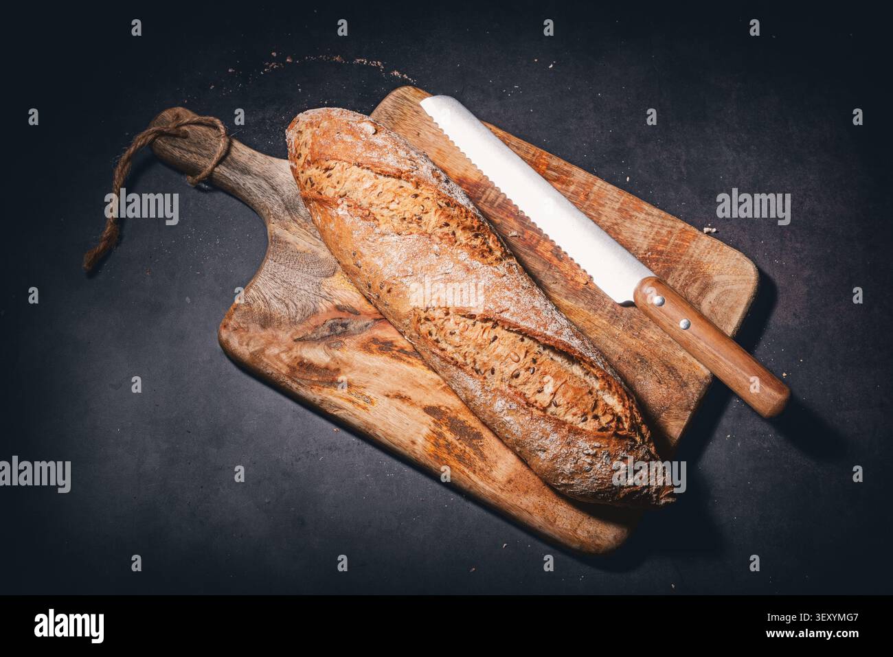 Freshly baked rustic bread baguette with seeds on wooden cutting board with knife Stock Photo