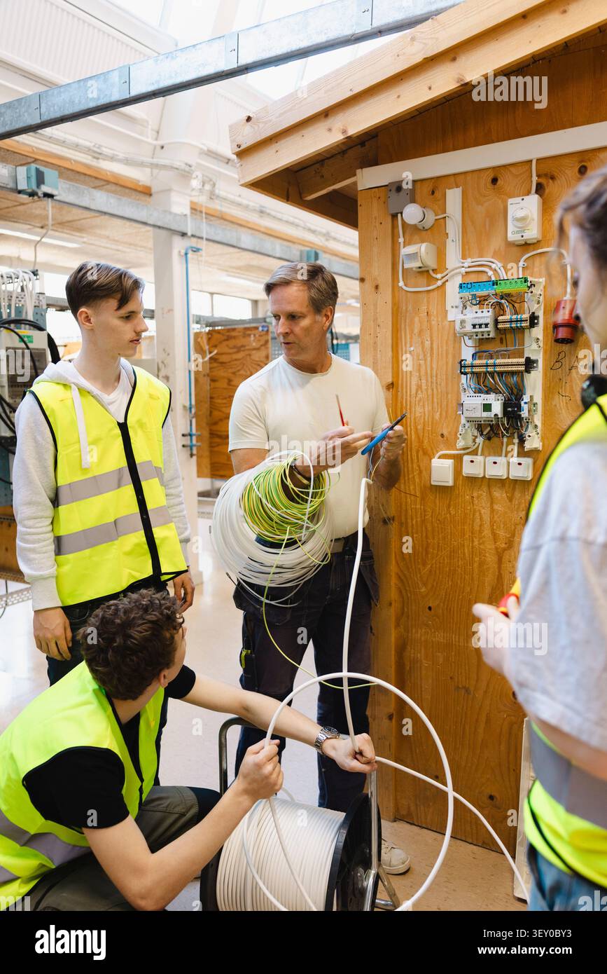 Experienced instructor demonstrating technical wiring techniques to young students in vocational workshop Stock Photo