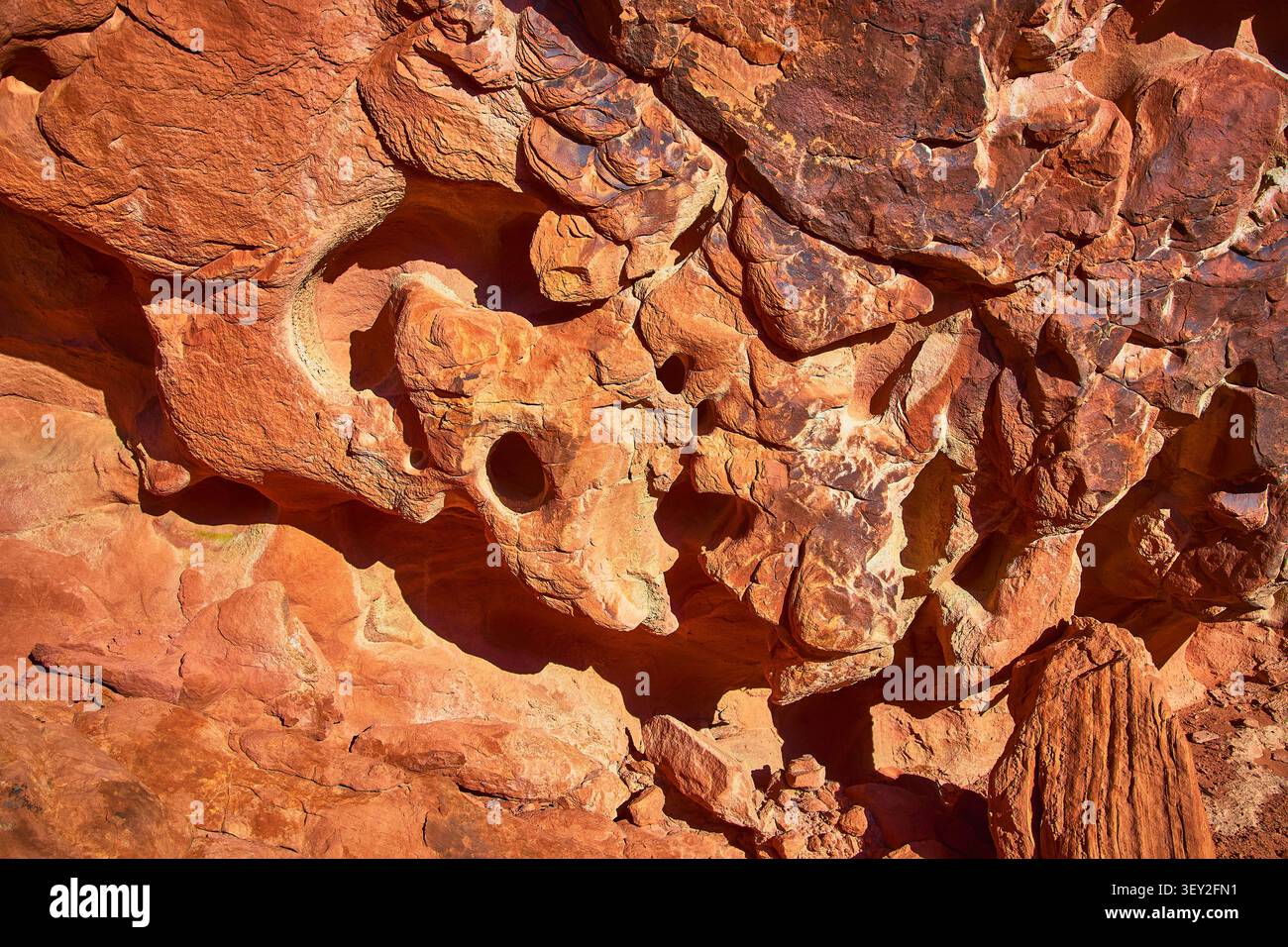 Textured Sandstone Rock Face with Erosion Holes and Sunlit Red Patterns Stock Photo