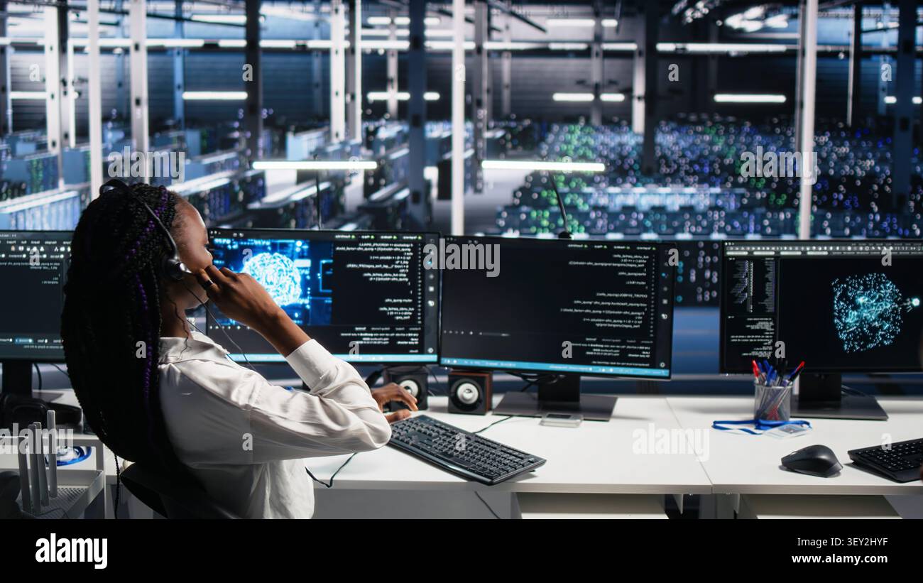 System administrator wears a headset in a server farm, using artificial intelligence troubleshooting to assist users. Stock Photo