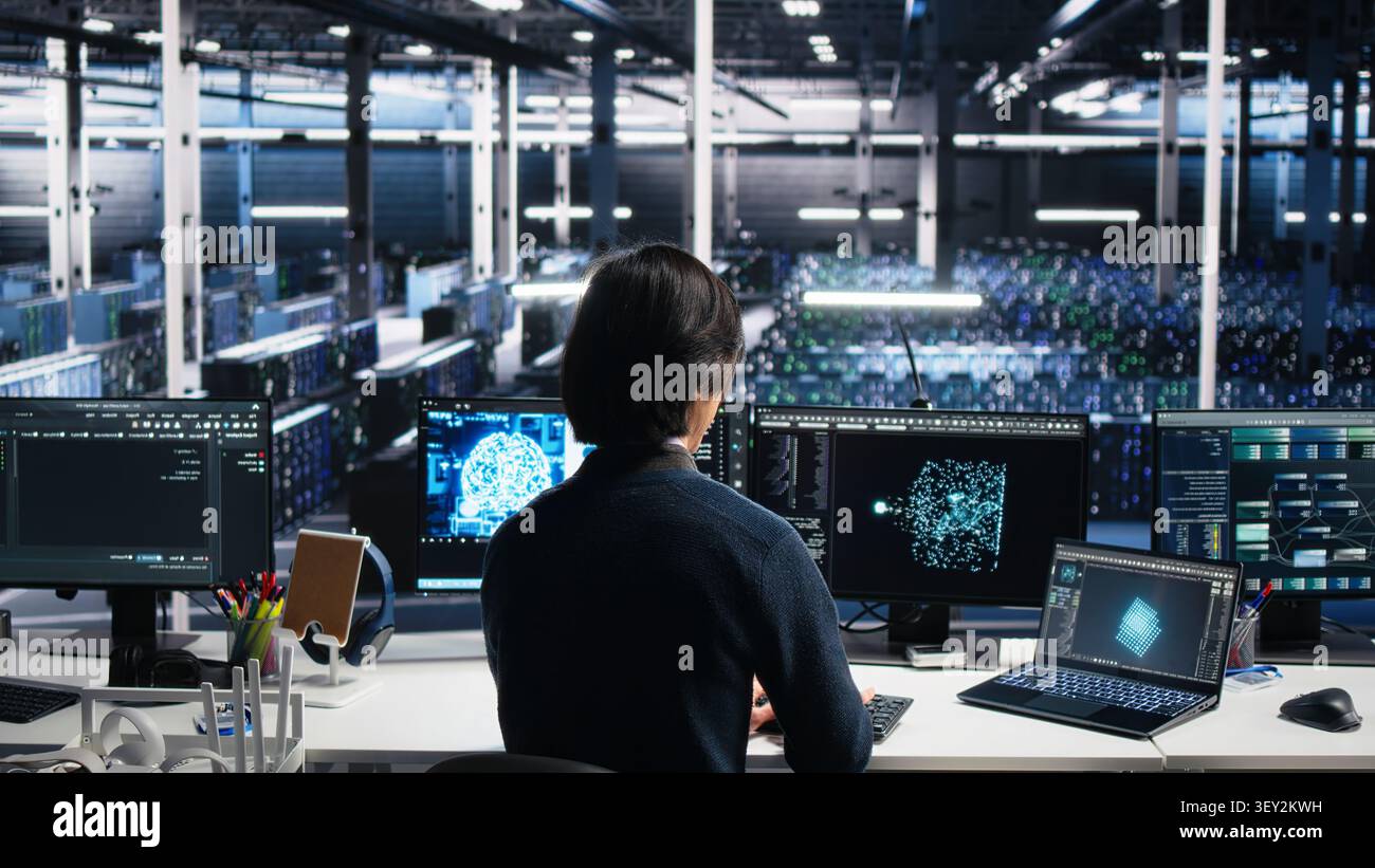 Computing facility system administrator managing AI systems for uptime and efficiency, while IT staff member working with AI technology on computer and notebook in computing hub. Stock Photo