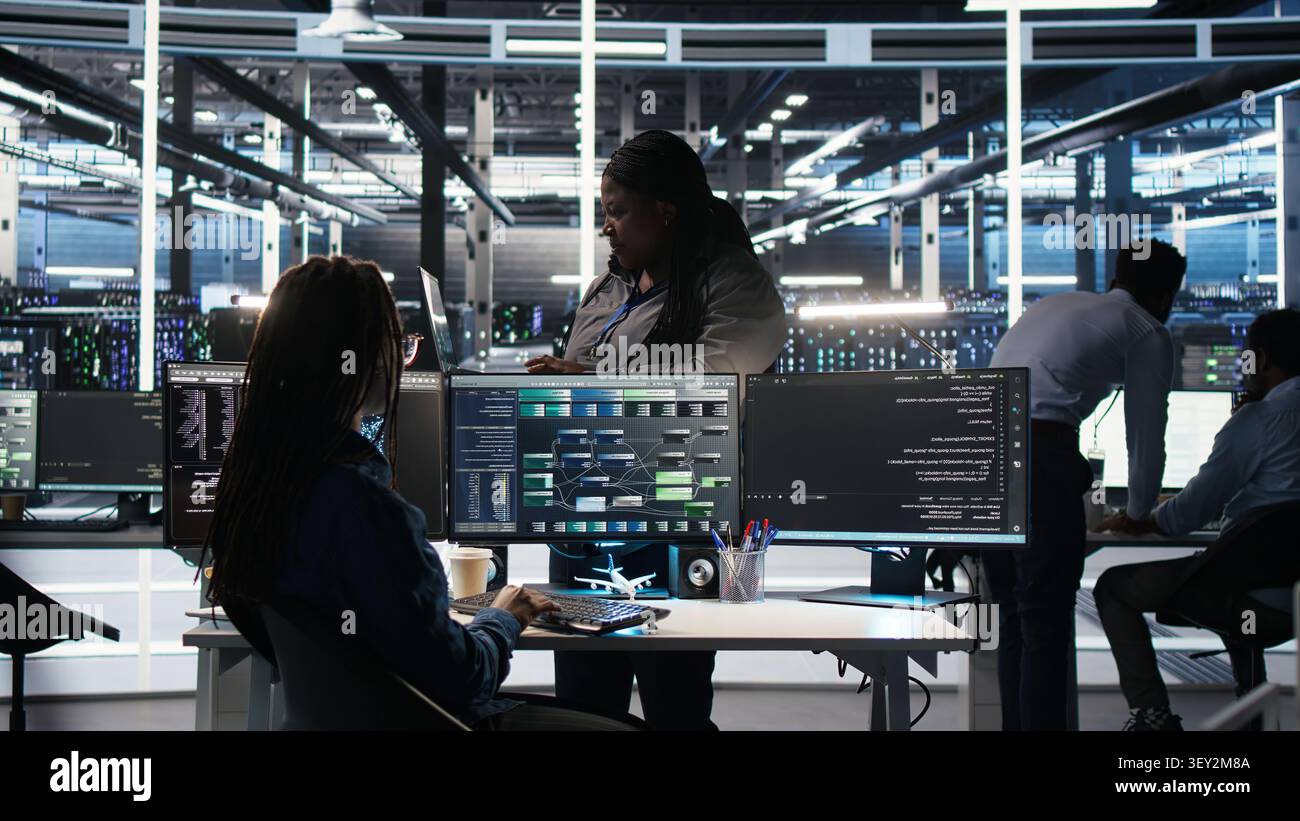 Computing facility team supervisor supervising IT technician working with visual programming system to assess datasets with team leader oversees IT specialist working with visual programming tools. Stock Photo